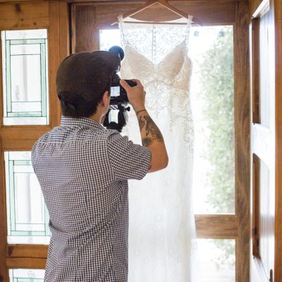 A young videographer shoots a beautiful wedding gown hanging in a doorway