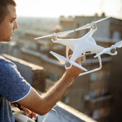 Young technician flying UAV drone with remote control on rooftop